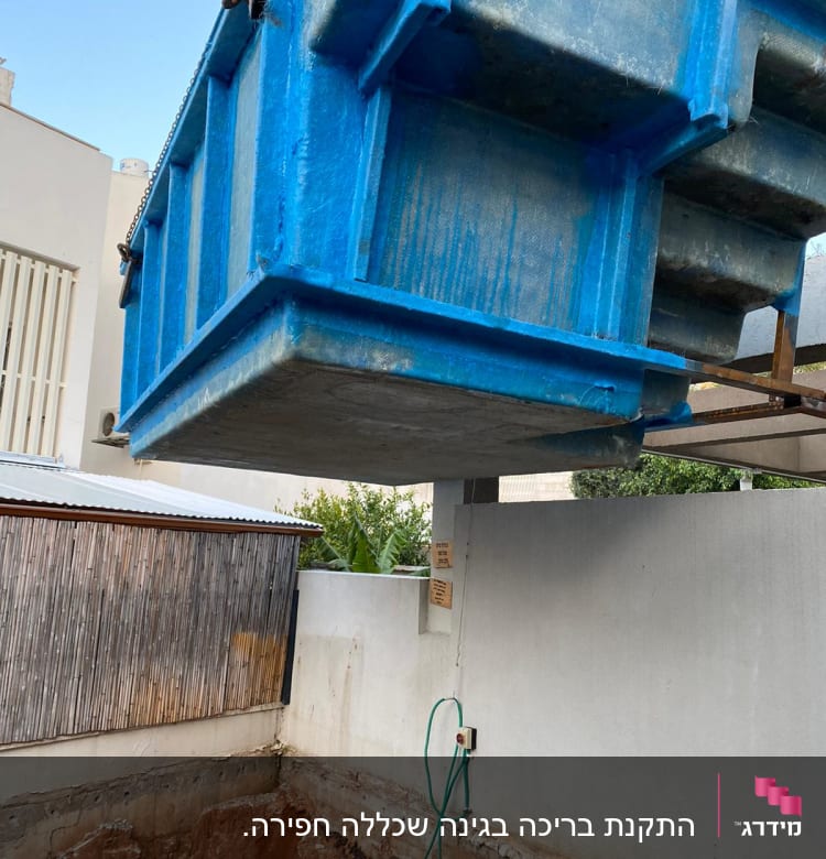 מכולה כחולה תלויה מעל חפירה באתר שיפוצים